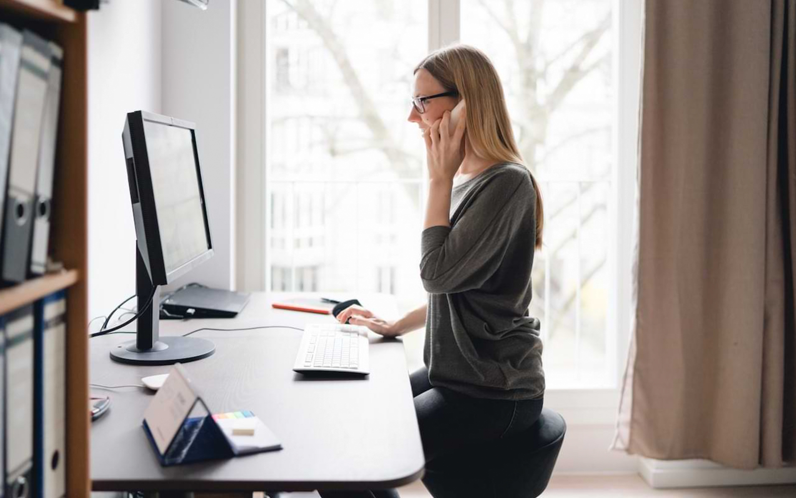 Eine Frau, die an ihrem Arbeitsplatz vor ihrem PC sitzt und telefoniert