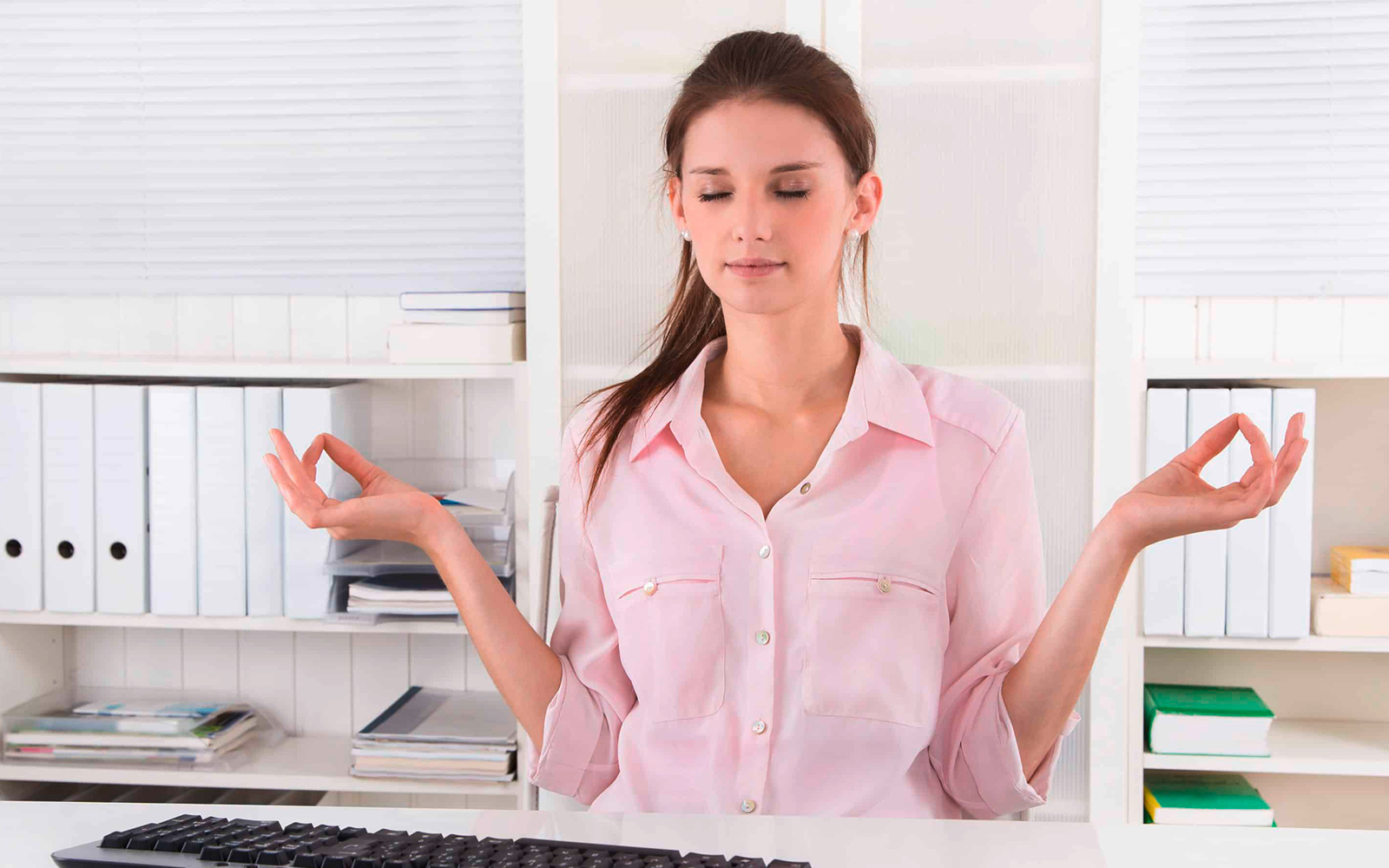 Eine weibliche Mitarbeiterin, die an ihrem Arbeitsplatz Meditationsübungen macht