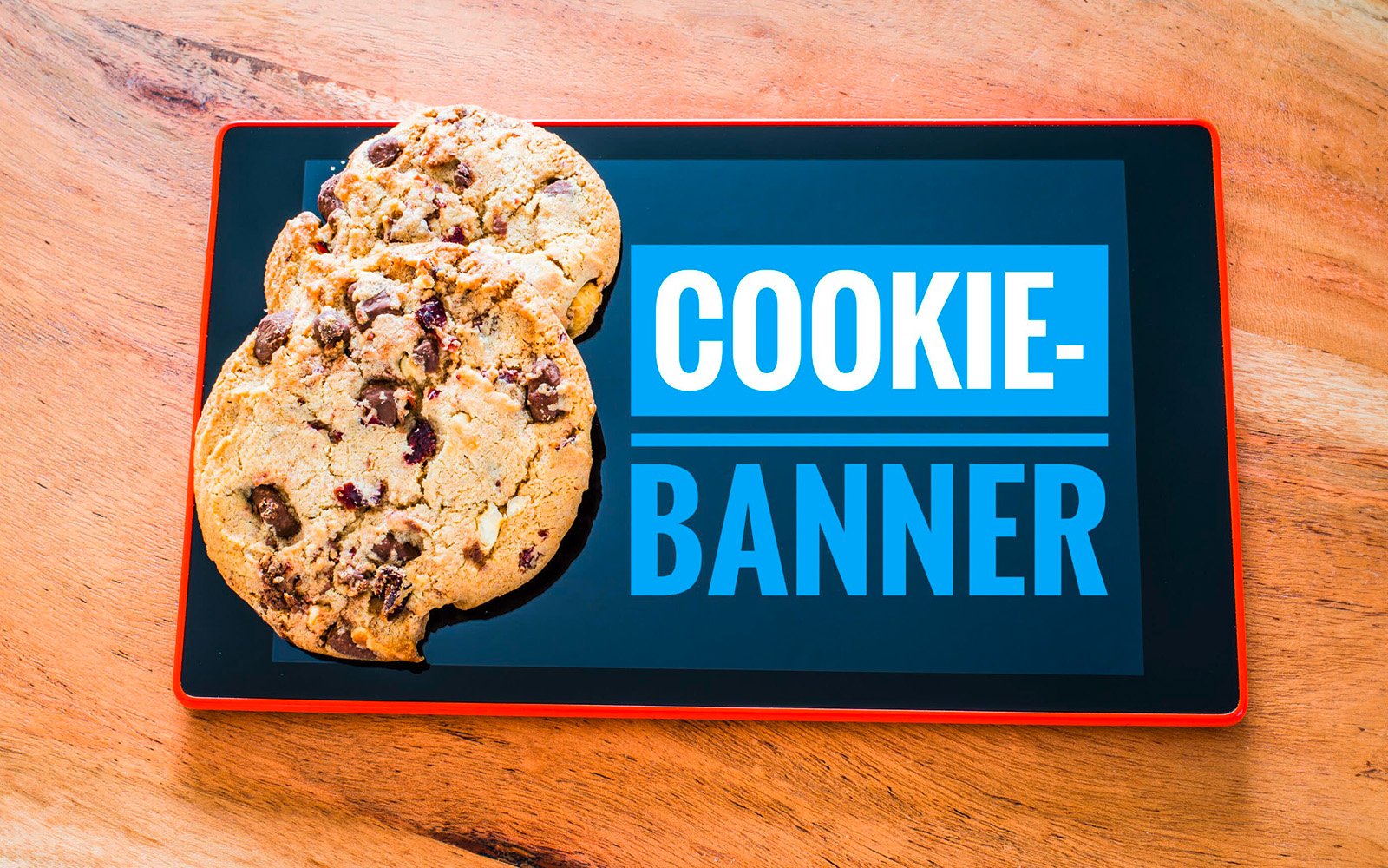 Ein Tablet, wo Cookiebanner drauf steht und echte Kekse daneben liegen.